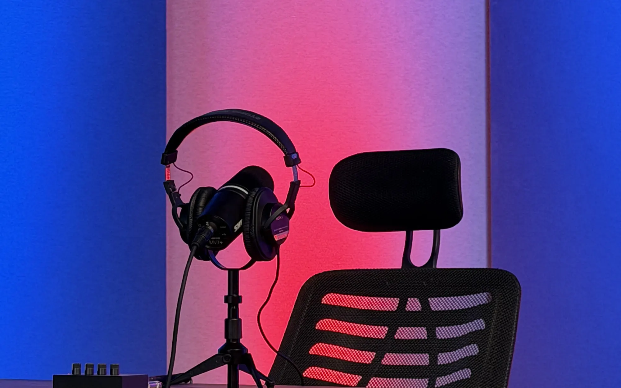 Auriculares Sony sobre un soporte junto a una silla de conducción, con luz roja y azul de fondo