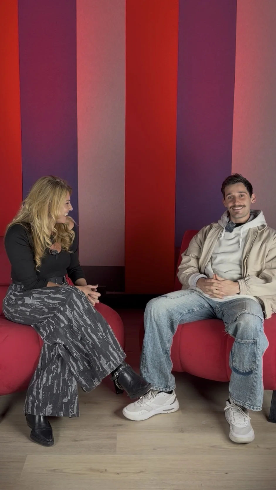 Dos personas conversando en los sillones rojos de NEXO Studios frente a los paneles verticales rojos y blancos