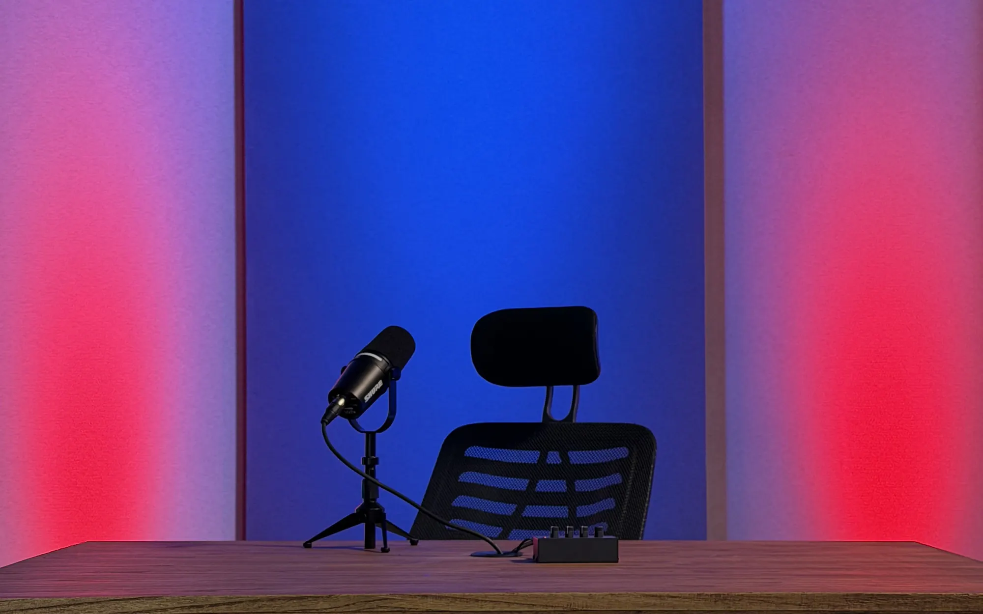 Set de NEXO Studios: paneles azules y rosados de fondo, mostrador de madera con micrófono Shure y silla de conducción