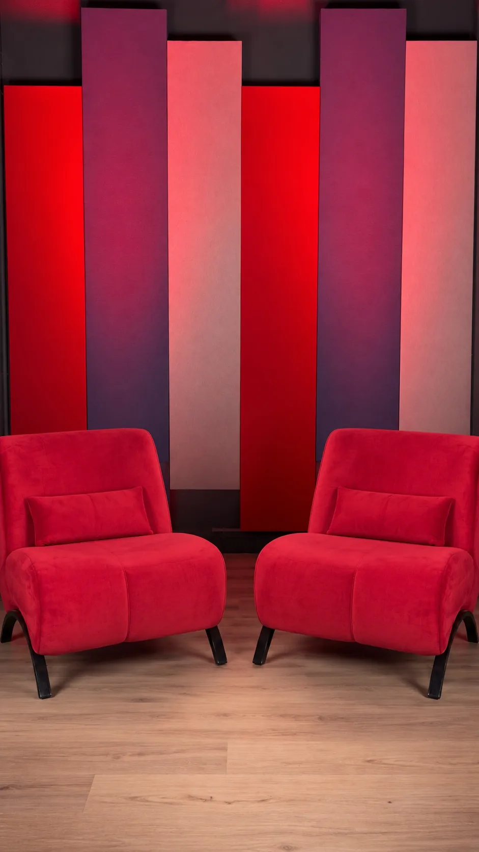 Dos sillones rojos vacíos frente a los paneles verticales rojos y blancos del live set de NEXO Studios