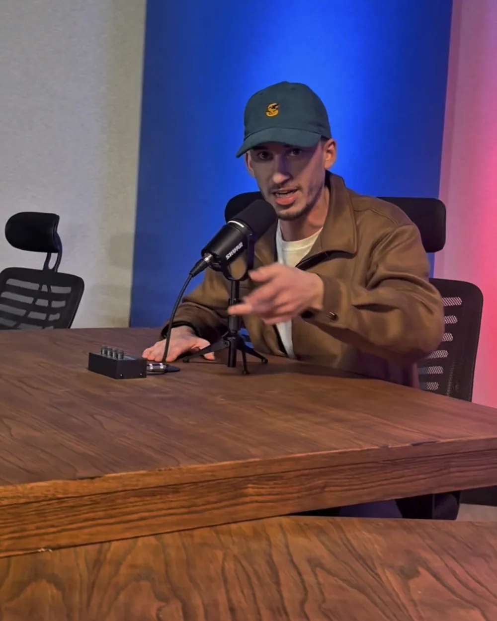 Conductor en la mesa de streaming de NEXO Studios con micrófono Shure y paneles azul y rojo